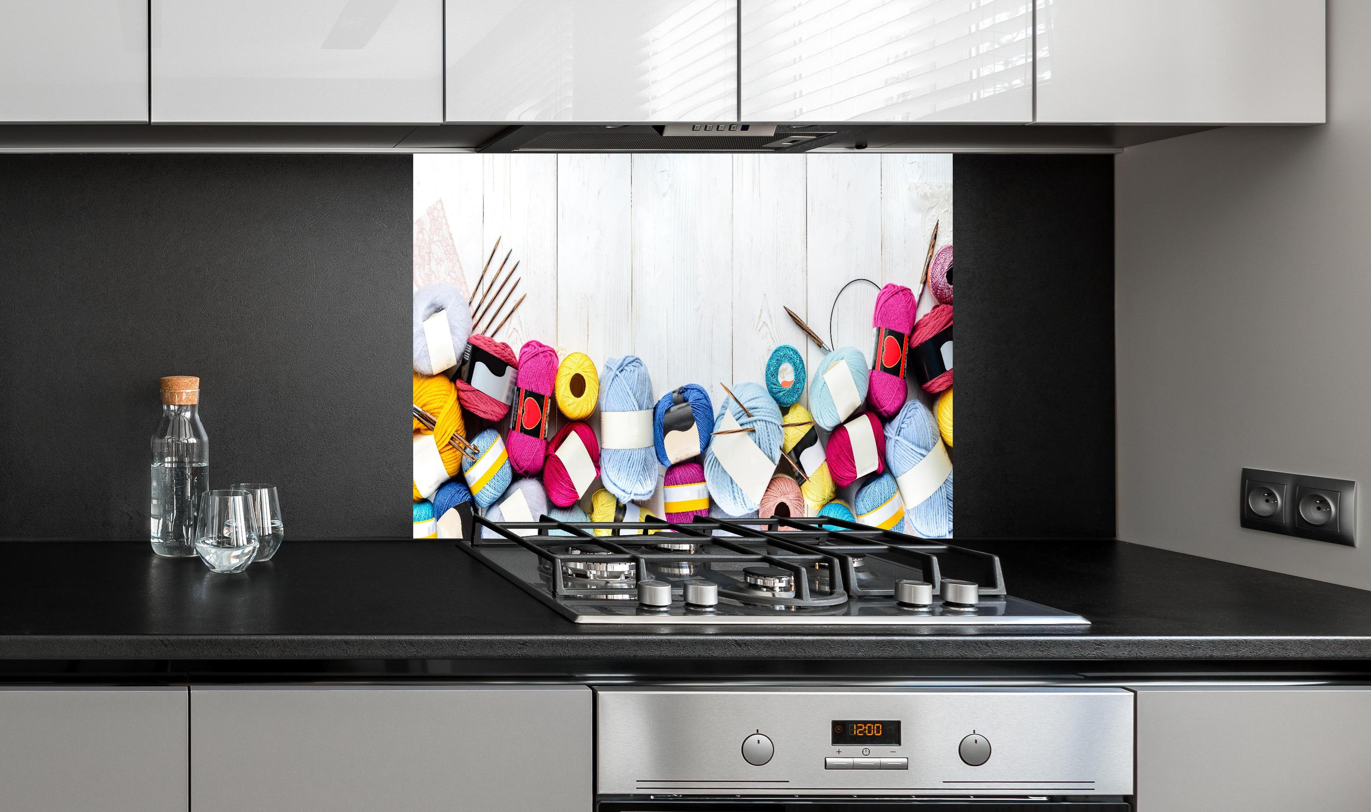 Spritzschutz - Wolle und Stricknadeln auf Holzhintergrund hinter einem Cerankochfeld zwischen Holz-Kochutensilien
