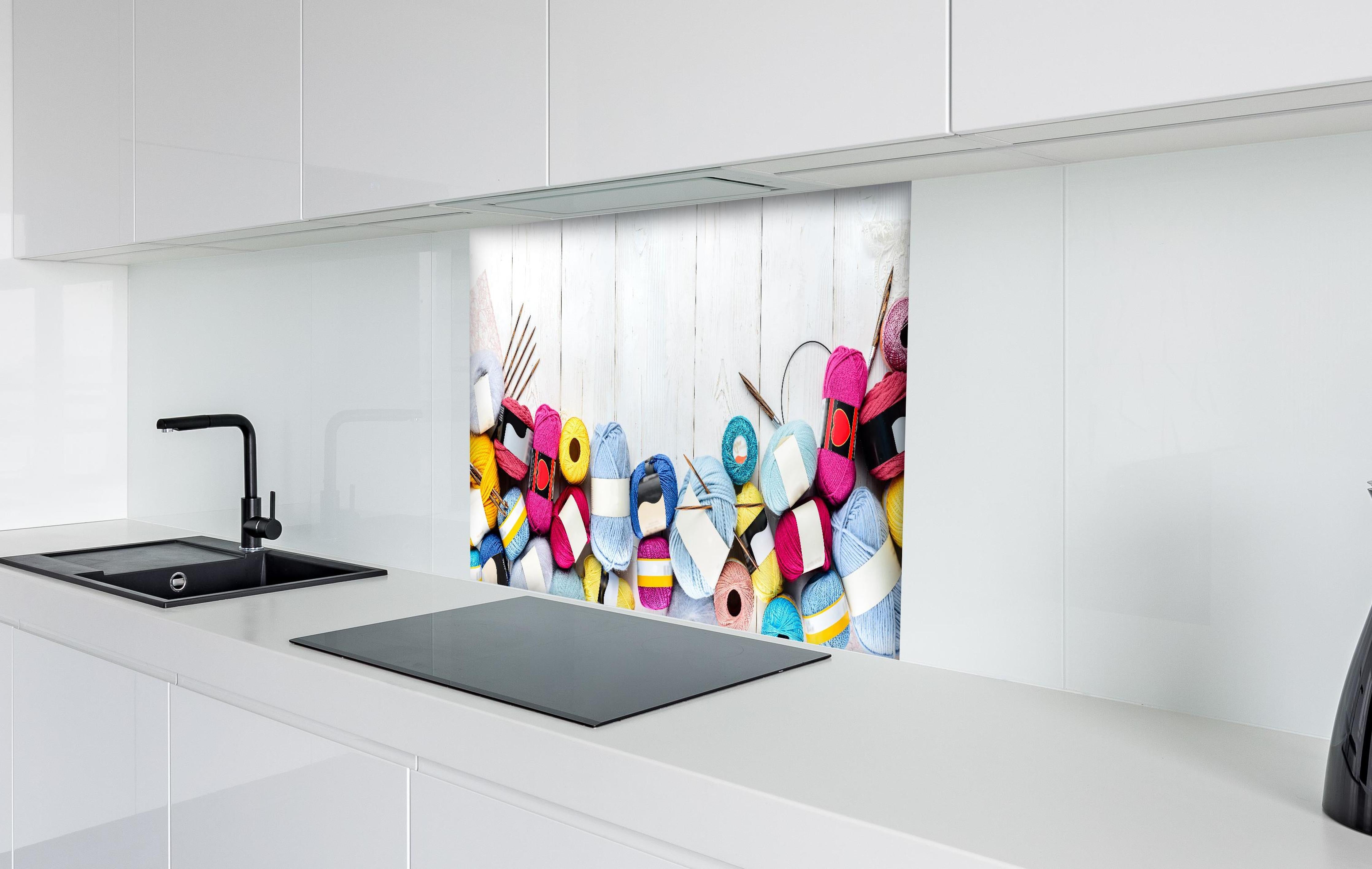 Spritzschutz - Wolle und Stricknadeln auf Holzhintergrund hinter einem Cerankochfeld zwischen Holz-Kochutensilien
