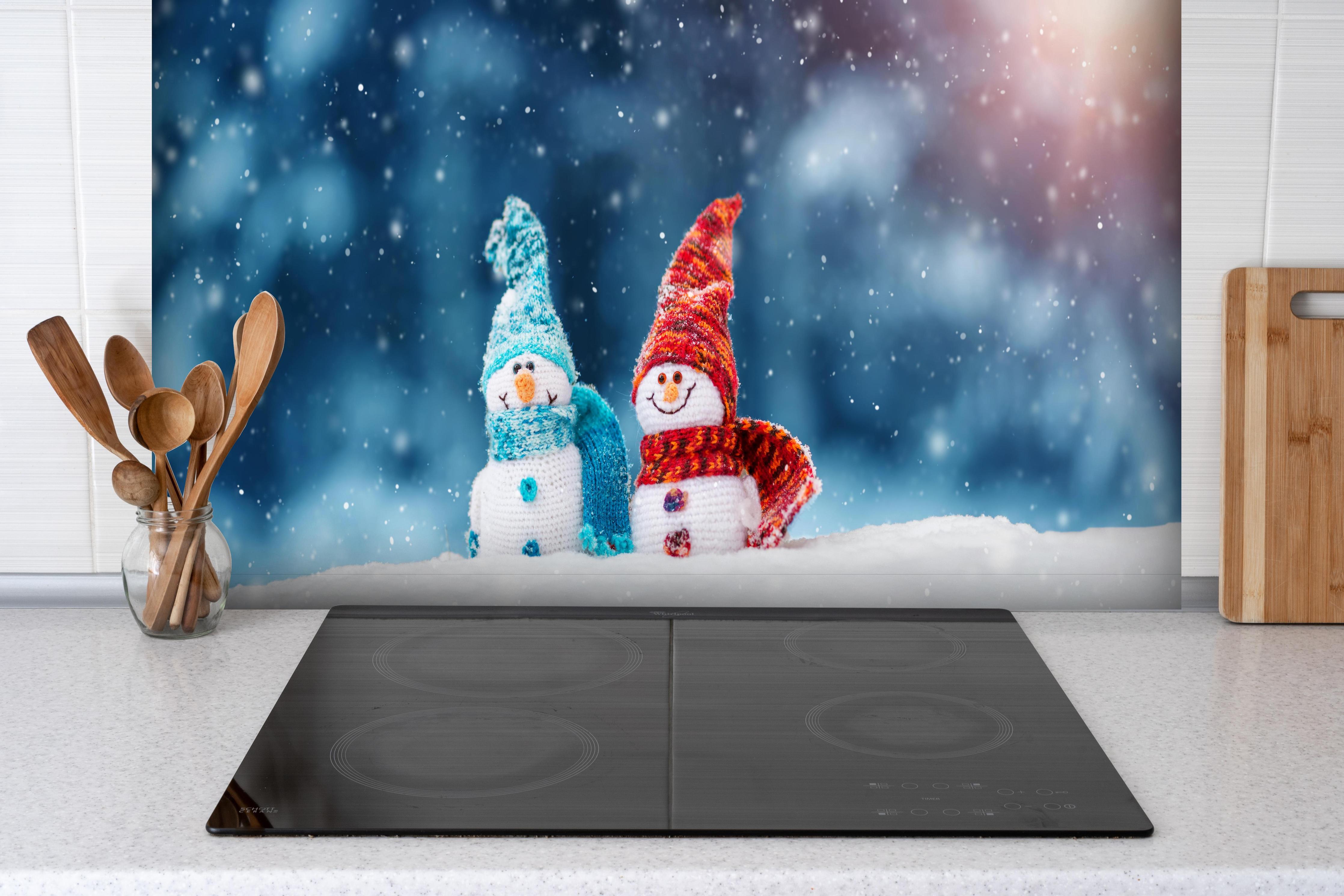 Spritzschutz - Zauberhafte Schneemänner auf weichem Schnee hinter einem Cerankochfeld zwischen Holz-Kochutensilien
