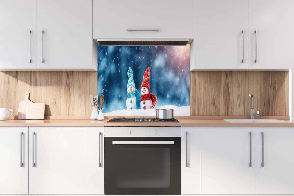 Spritzschutz - Zauberhafte Schneemänner auf weichem Schnee hinter einem Cerankochfeld zwischen Holz-Kochutensilien
