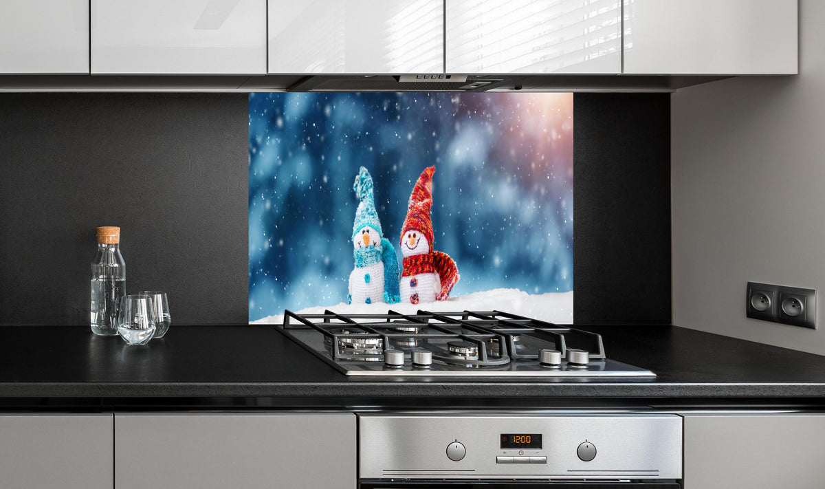 Spritzschutz - Zauberhafte Schneemänner auf weichem Schnee hinter einem Cerankochfeld zwischen Holz-Kochutensilien
