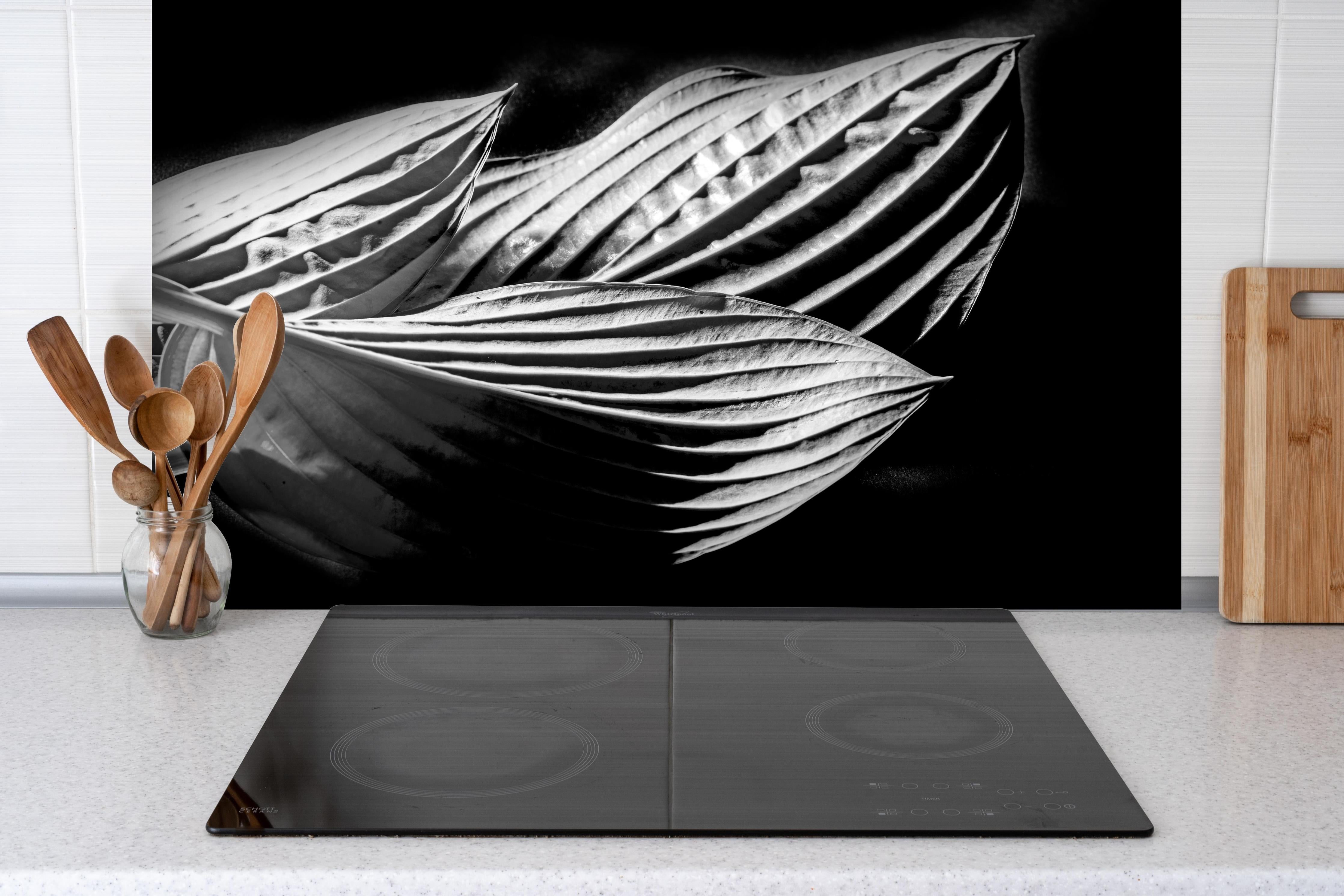 Spritzschutz - drei Blätter auf dunklem Hintergrund hinter einem Cerankochfeld zwischen Holz-Kochutensilien

