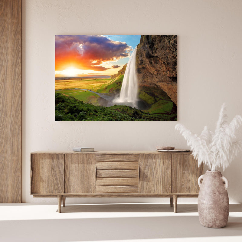 Wandbild -  Seljalandsfoss Wasserfall bei Sonnenuntergang über Holzkommode hinter dekorativer Zimmerpflanze