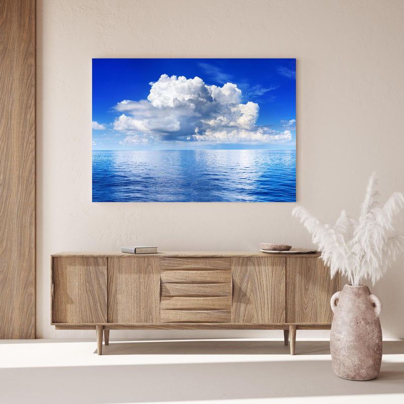 Wandbild - Wolkenkulisse über dem Ozean über Holzkommode hinter dekorativer Zimmerpflanze