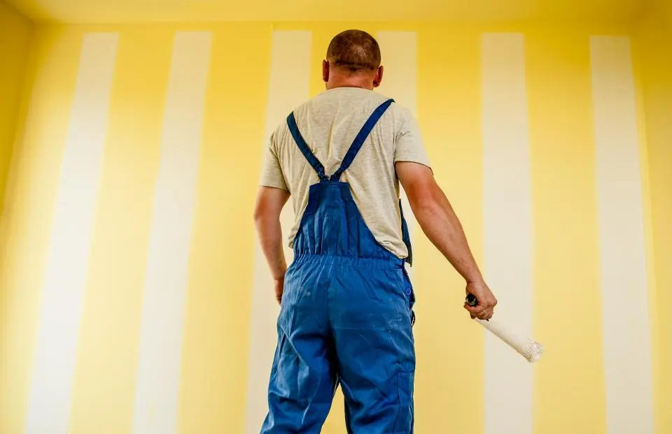 Maler im Blaumann vor frisch gestrichener Wand